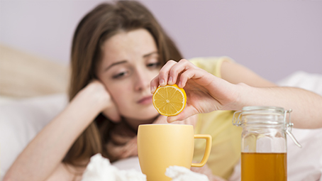 Ill woman laying on bed, adding lemon juice to tea